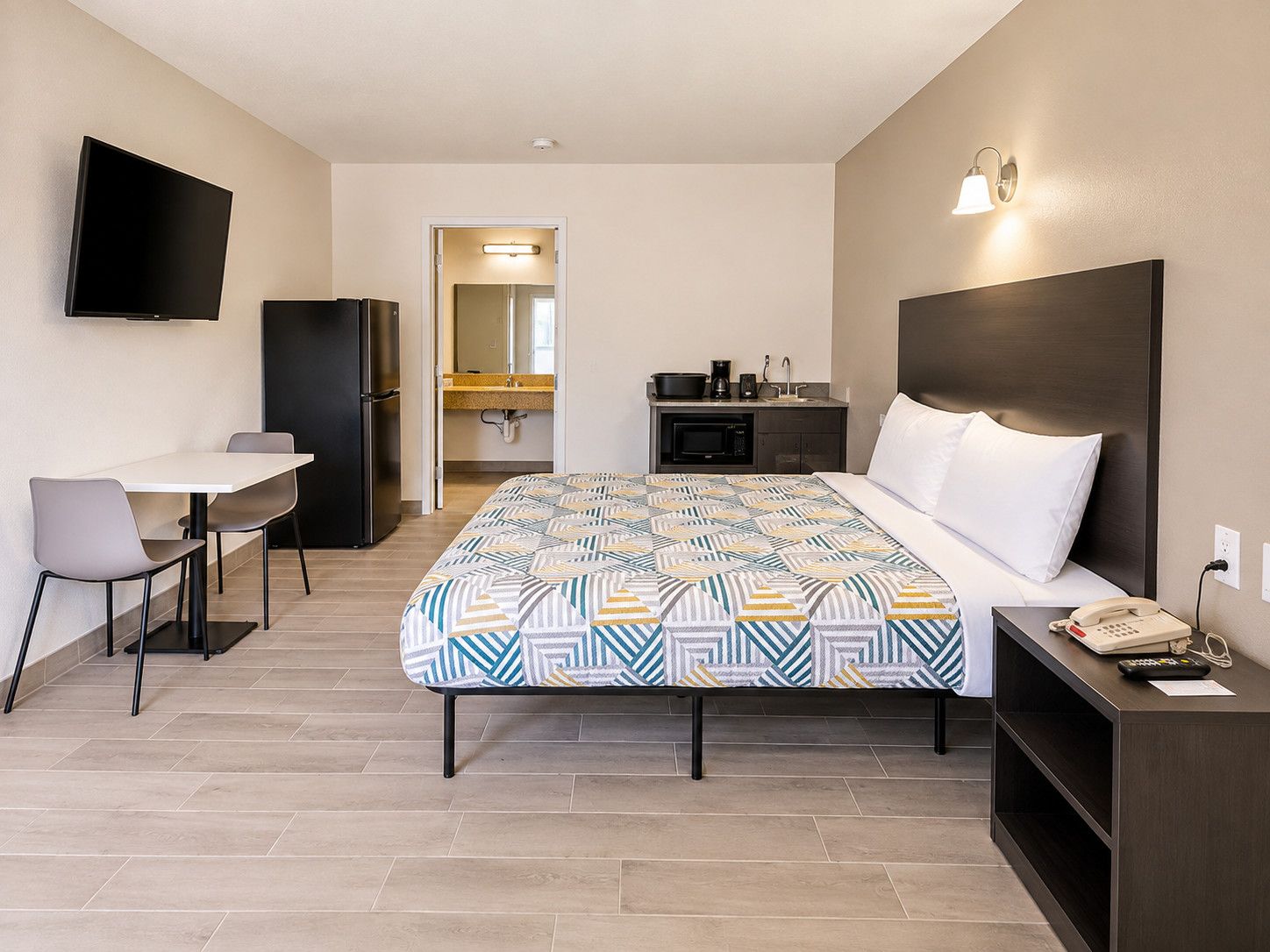 A hotel room with a bed, a desk, a chair, a TV, a microwave, a coffee maker, and a telephone.