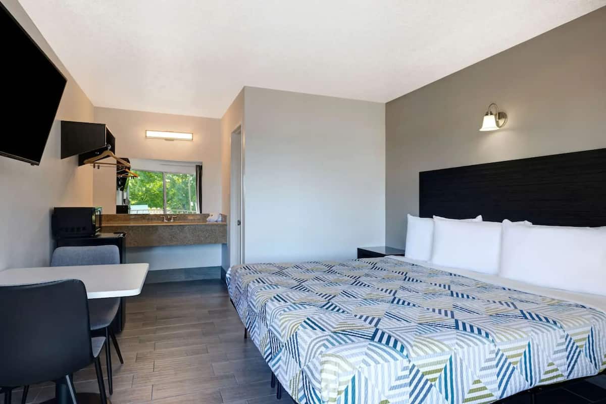 A modern hotel room with a large bed, a desk, and a TV mounted on the wall.