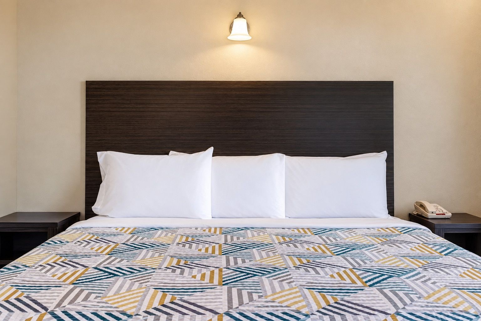 A hotel room with a bed, a nightstand, a telephone, and a wall-mounted light fixture.
