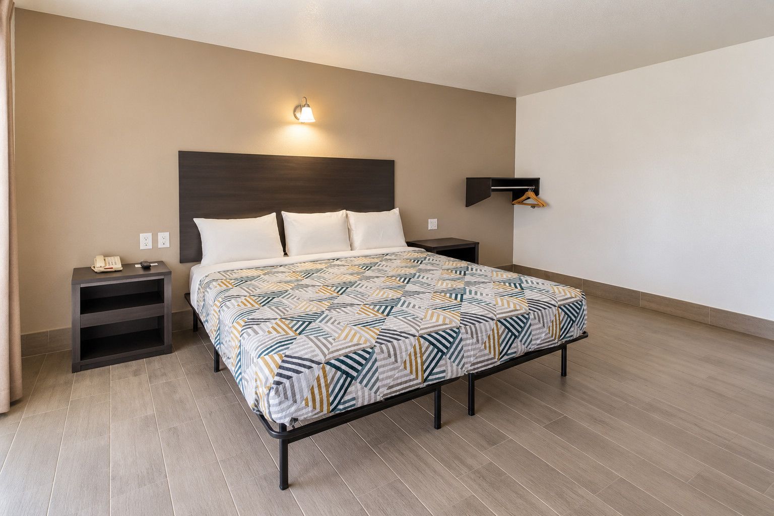 Ein Hotelzimmer mit Bett, Nachttischen, einer Wandlampe und Holzboden.