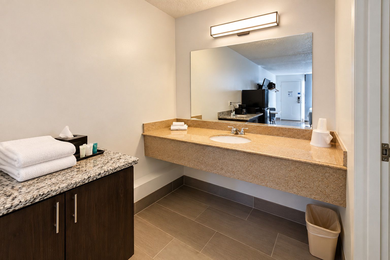 Un baño moderno con encimera de granito, lavabo, espejo, toallero y cubo de basura.