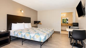 Habitación de hotel con cama, mesita de noche, escritorio, silla, televisión y un baño pequeño.