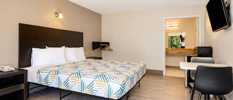 A hotel room with a bed, bedside table, desk, chair, TV, and a small bathroom area.