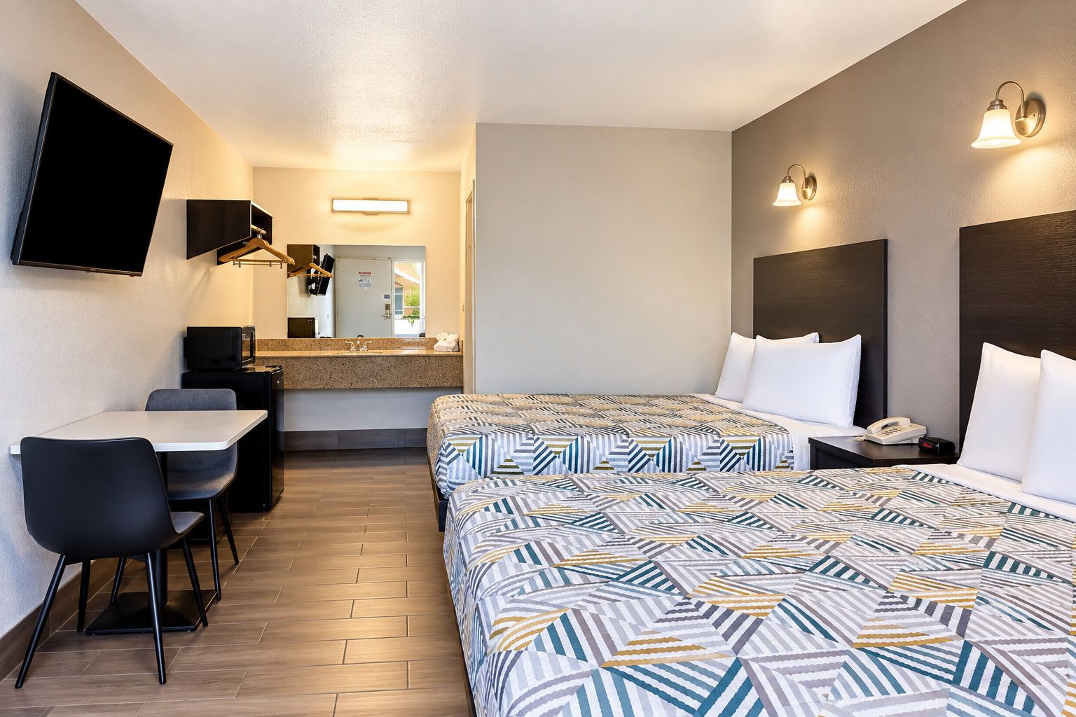 Habitación de hotel con cama, escritorio, sillas, espejo y teléfono.