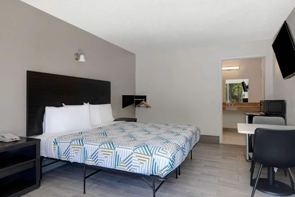 A hotel room with a bed, bedside table, chair, desk, TV, and a mirror.
