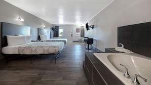 A hotel room with two beds, a large bathtub, a desk, and a chair. - Crestview Inn (Branson West)