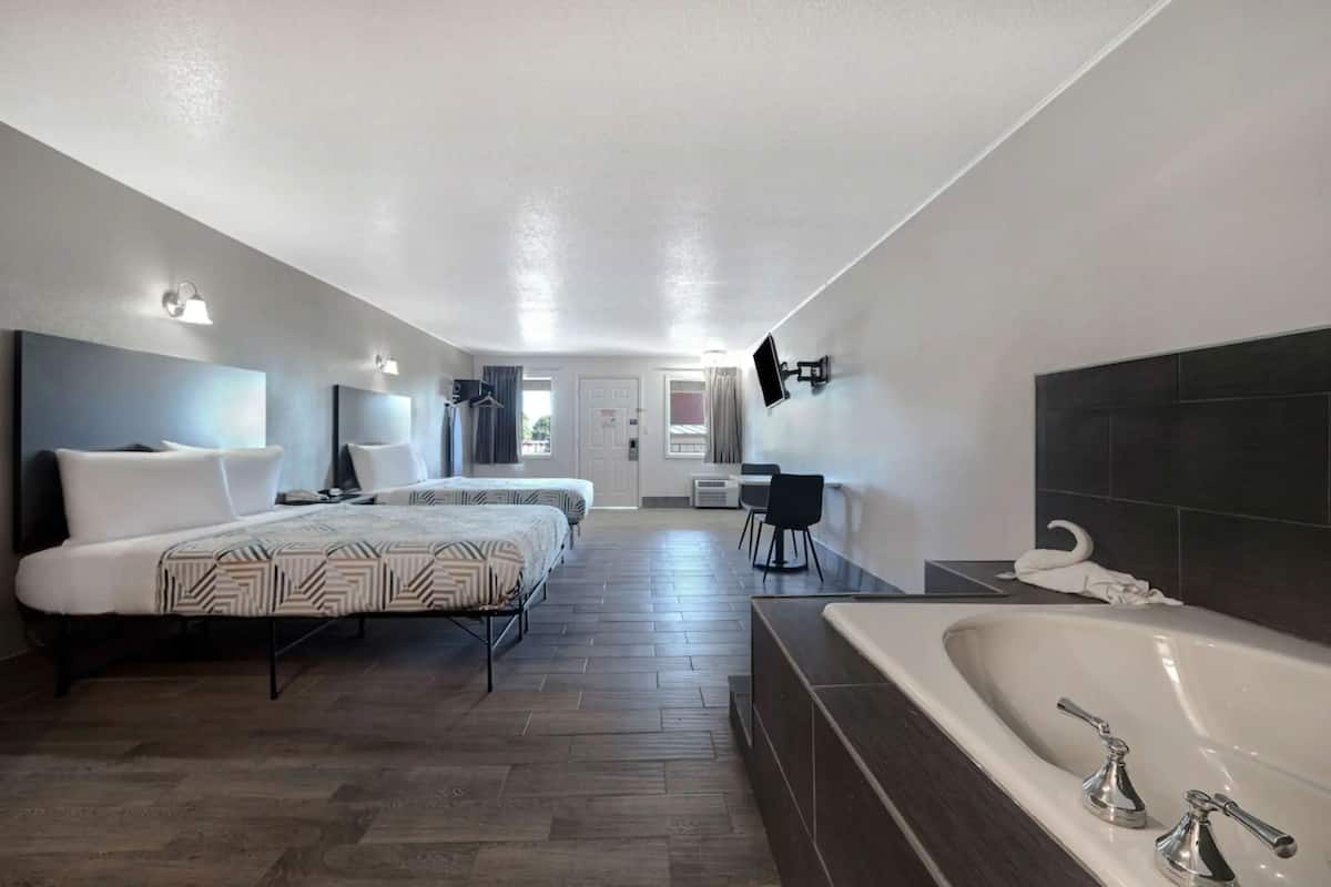 A hotel room with two beds, a large bathtub, a desk, and a chair.
