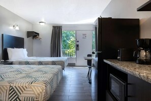 Une chambre d’hôtel avec deux lits, une kitchenette, un coin repas et une porte-fenêtre coulissante donnant sur l’extérieur.