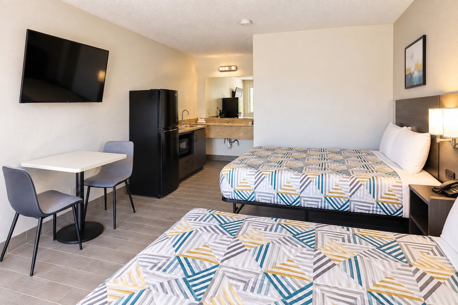 A hotel room with a bed, a desk, a chair, a refrigerator, a television, and a bathroom.