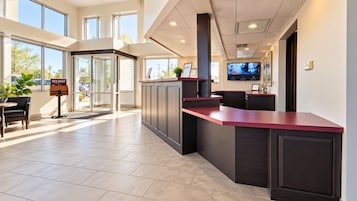 A hotel reception area with a modern design, including a reception desk, seating area, and a large window providing a view of the outdoors.