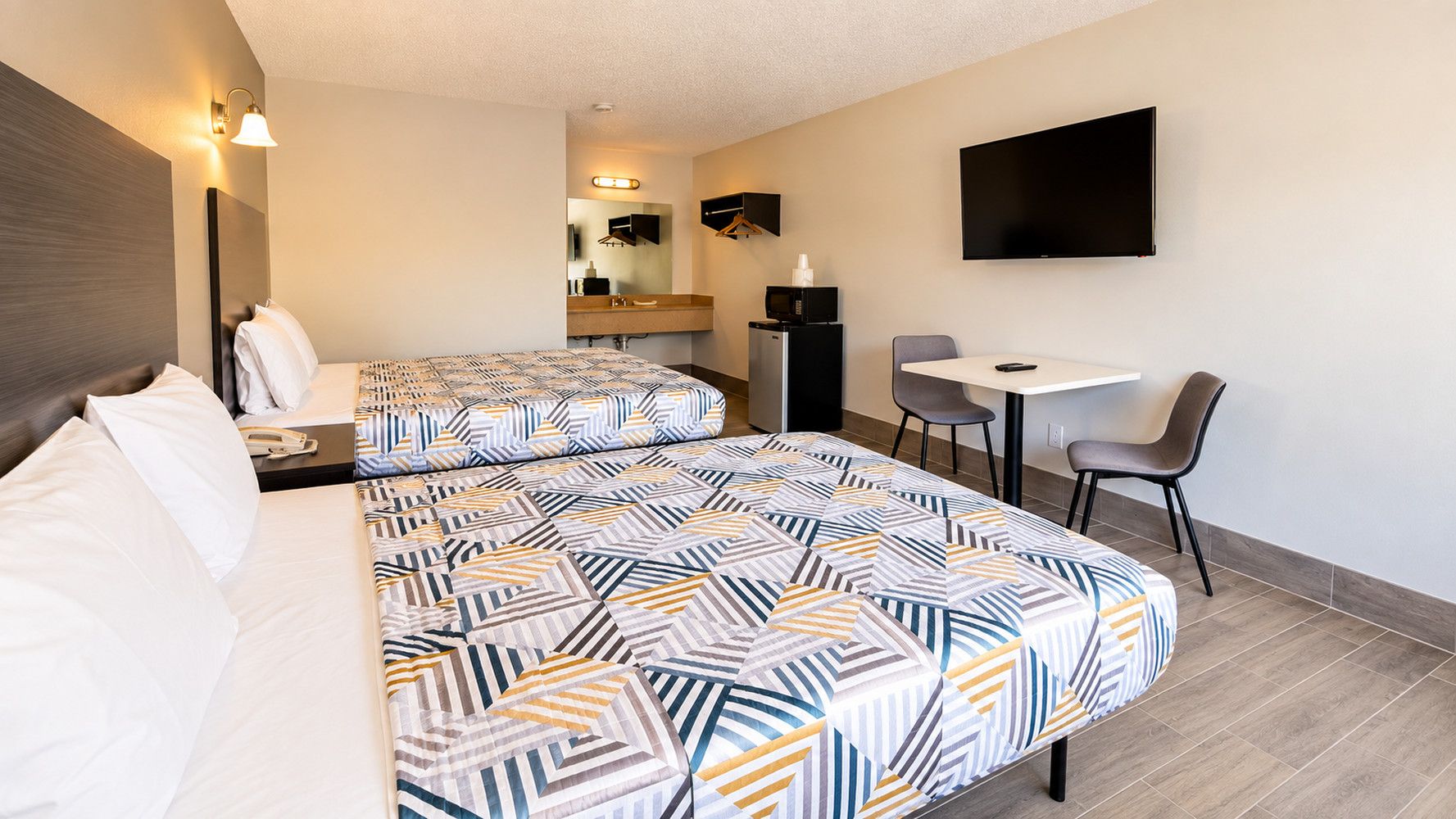 A hotel room with a bed, bedside table, lamp, TV, and a small desk with a chair.