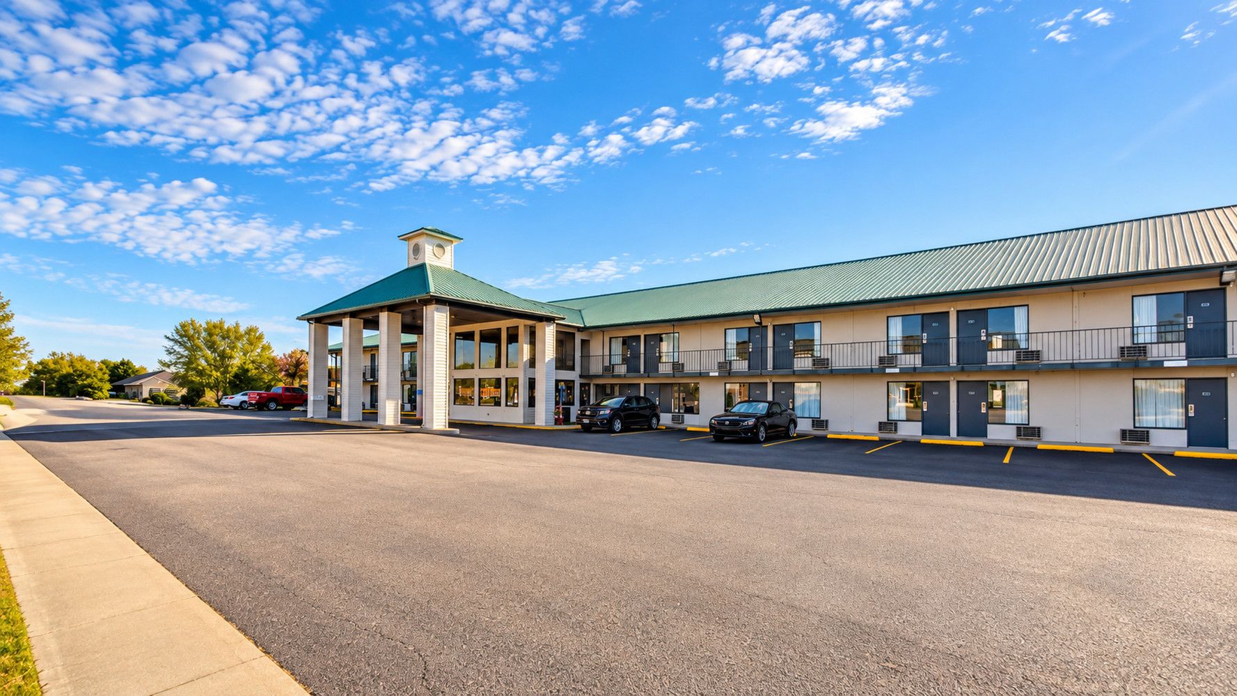 Un motel con vestíbulo central, varias habitaciones y zona de estacionamiento.
