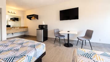 Una camera d'albergo con due letti, un tavolino con sedie, una TV a parete, un minibar e uno specchio con luci.