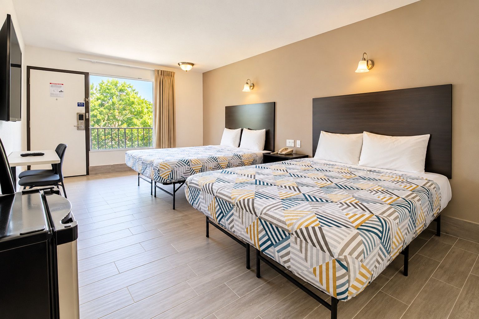 Een hotelkamer met twee bedden, een bureau en een balkon.