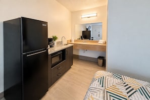 Una kitchenette compacta con refrigerador negro, microondas, cafetera y pileta.