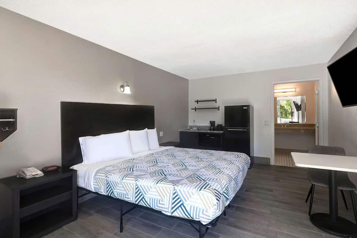 A modern hotel room with a bed, bedside table, desk, and a TV.