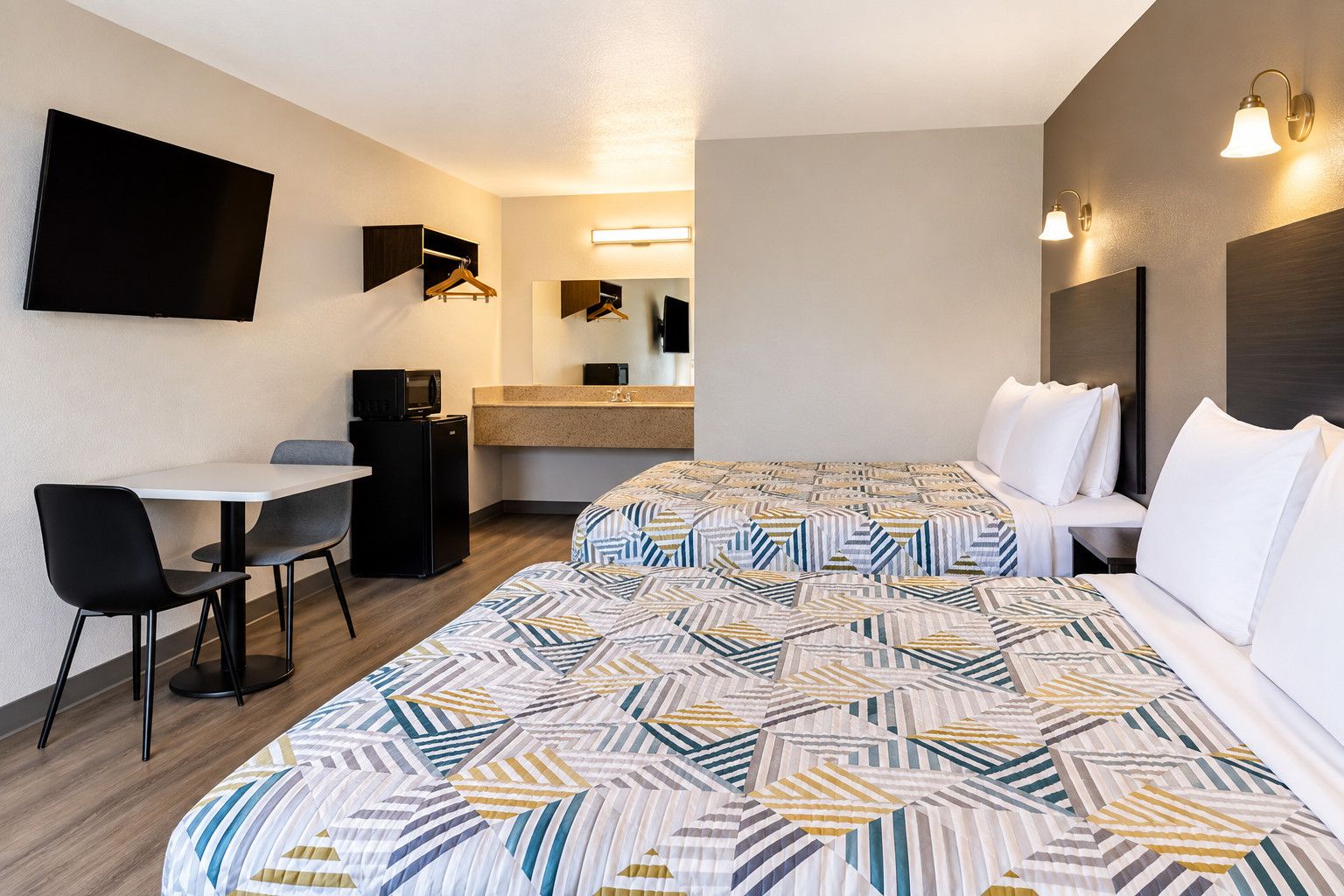 Et hotelværelse med seng, skrivebord, stol, mikrobølgeovn og fjernsyn.