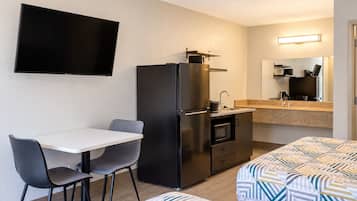 Une chambre d’hôtel compacte comprenant un coin cuisine, un téléviseur à écran plat fixé au mur, une table à manger avec deux chaises et un lit avec une literie à motifs.