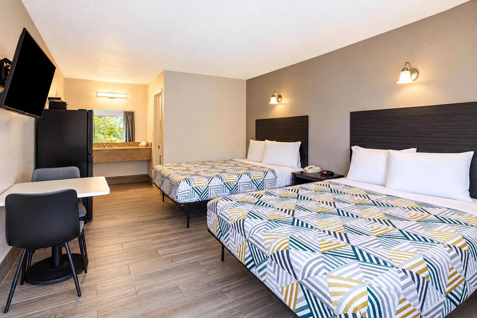 A hotel room with two beds, a desk, a chair, a TV, and a window with curtains.