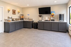A modern kitchen with grey cabinets, a flat-screen TV, and a coffee station.