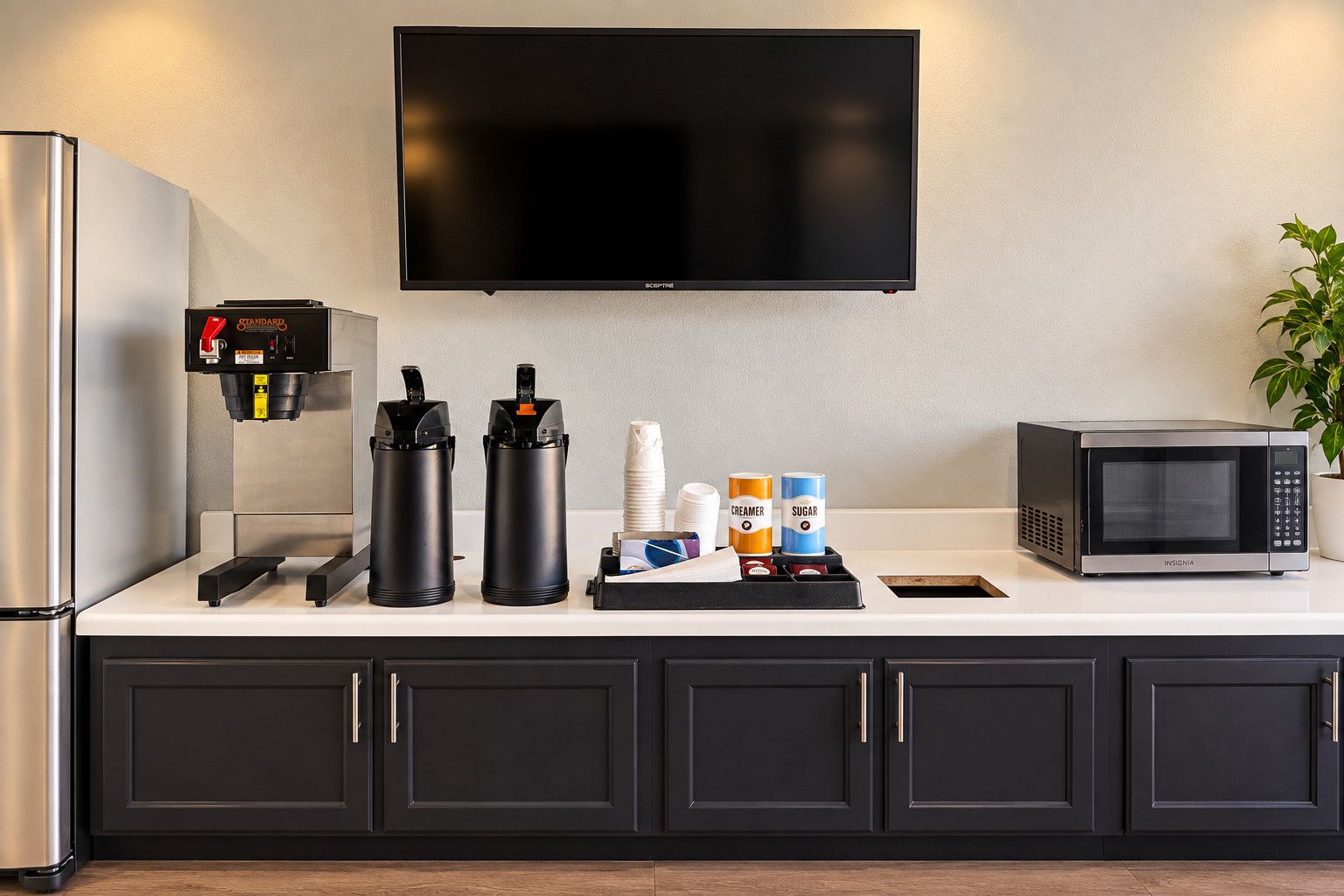 Een kitchenette met een koffieapparaat, een magnetron en een koelkast.