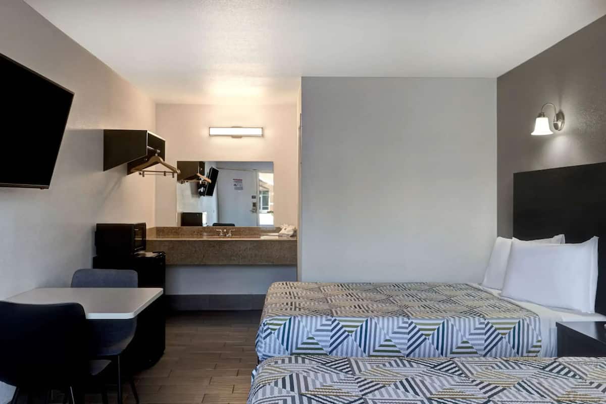 A hotel room with a bed, a desk, a chair, a TV, and a bathroom visible through an open door.