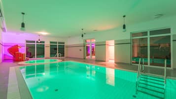 An indoor swimming pool with clear water, a ladder, and a red chair near the entrance.