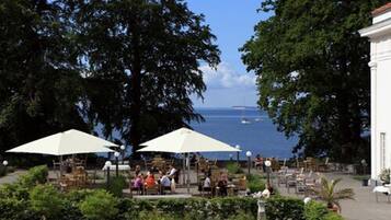 An outdoor seating area with umbrellas, tables, and chairs, overlooking a body of water.