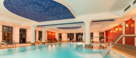 Una piscina interior con techo estrellado, sillas de descanso y una pared de acento roja.