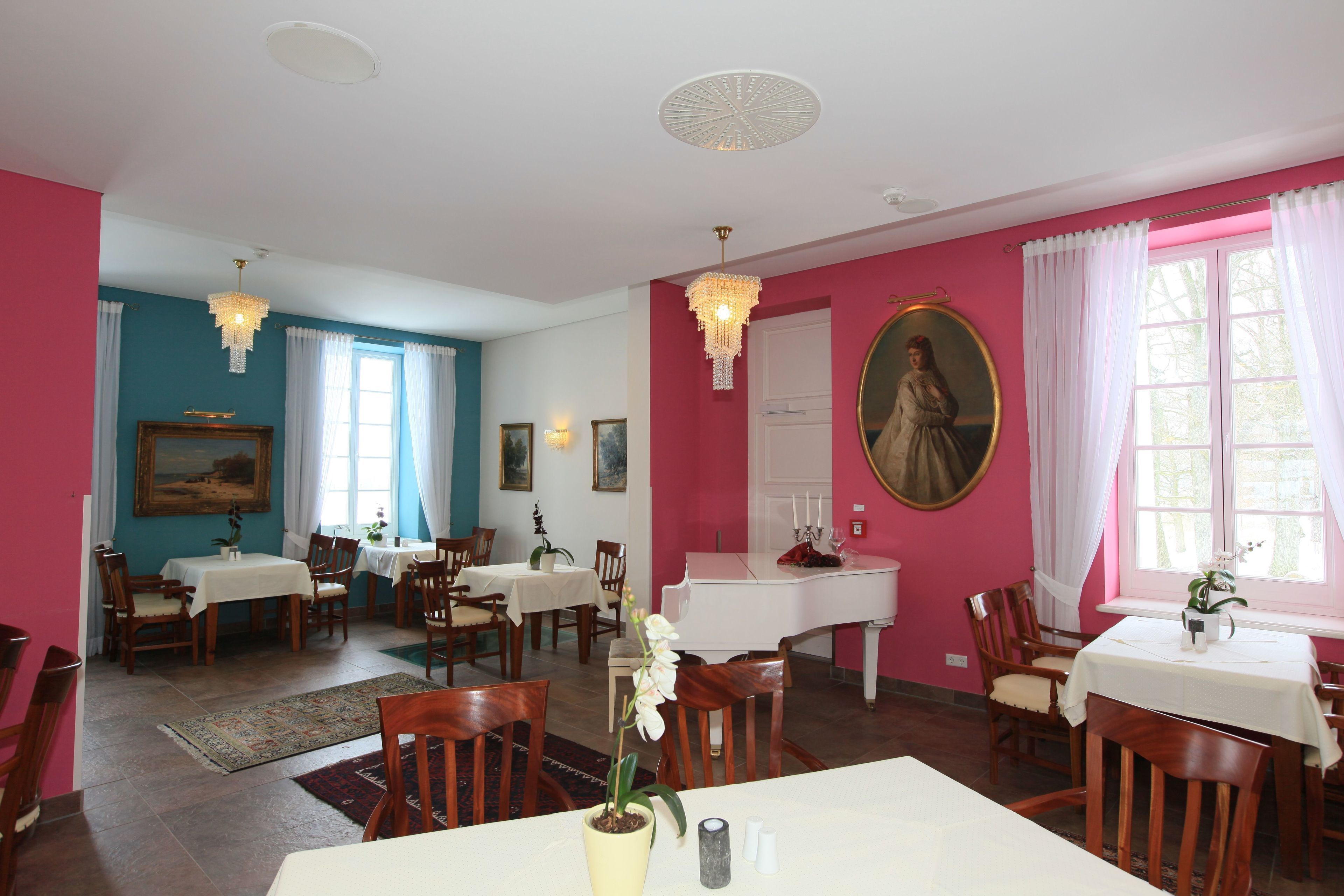 A dining area with multiple tables and chairs, a piano, and a painting on the wall.