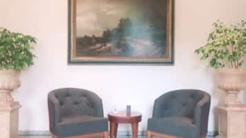 Dos sillones enfrentados con una pequeña mesa redonda entre ellos, un cuadro enmarcado en la pared y dos grandes macetas con plantas.