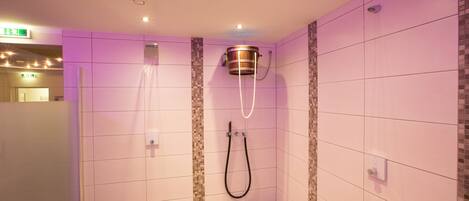 Een moderne badkamer met roze betegelde muren, een douchegedeelte met een houten badkuip en een zichtbaar vluchtroutebord.