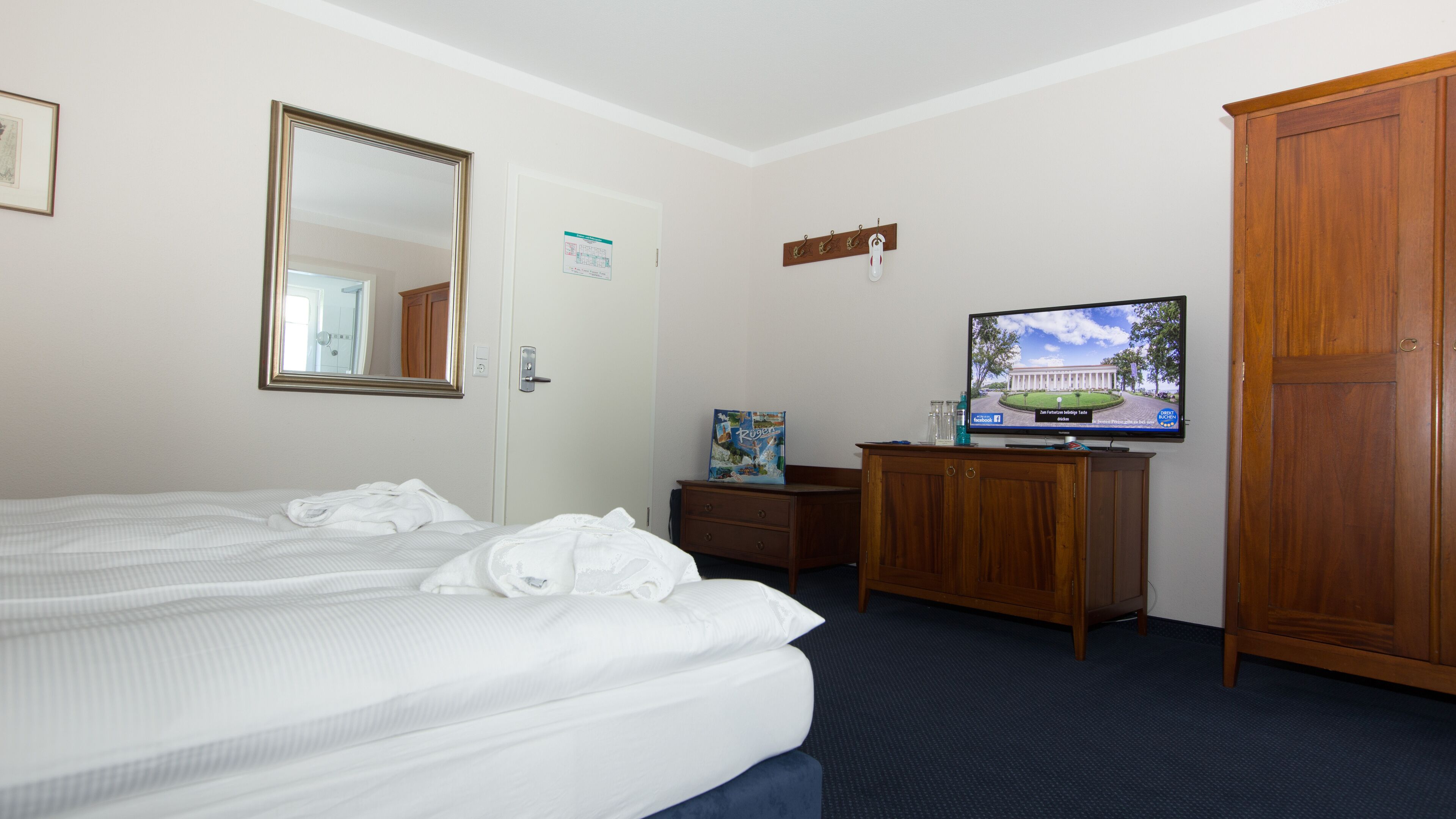 Una habitación de hotel con cama, cómoda, televisor y armario.
