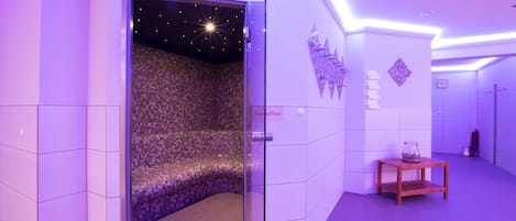 Un spa moderno con pared de mosaicos, una pequeña mesa de madera y una lámpara de techo que simula un cielo estrellado.