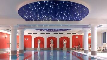A modern indoor swimming pool with a starry ceiling, red walls, and white columns.
