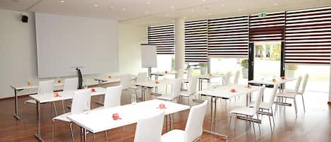 Un salón de conferencias con mesas y sillas blancas, un proyector y una pizarra.