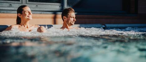 Una pareja en un jacuzzi con paredes de madera y ventanas amplias.