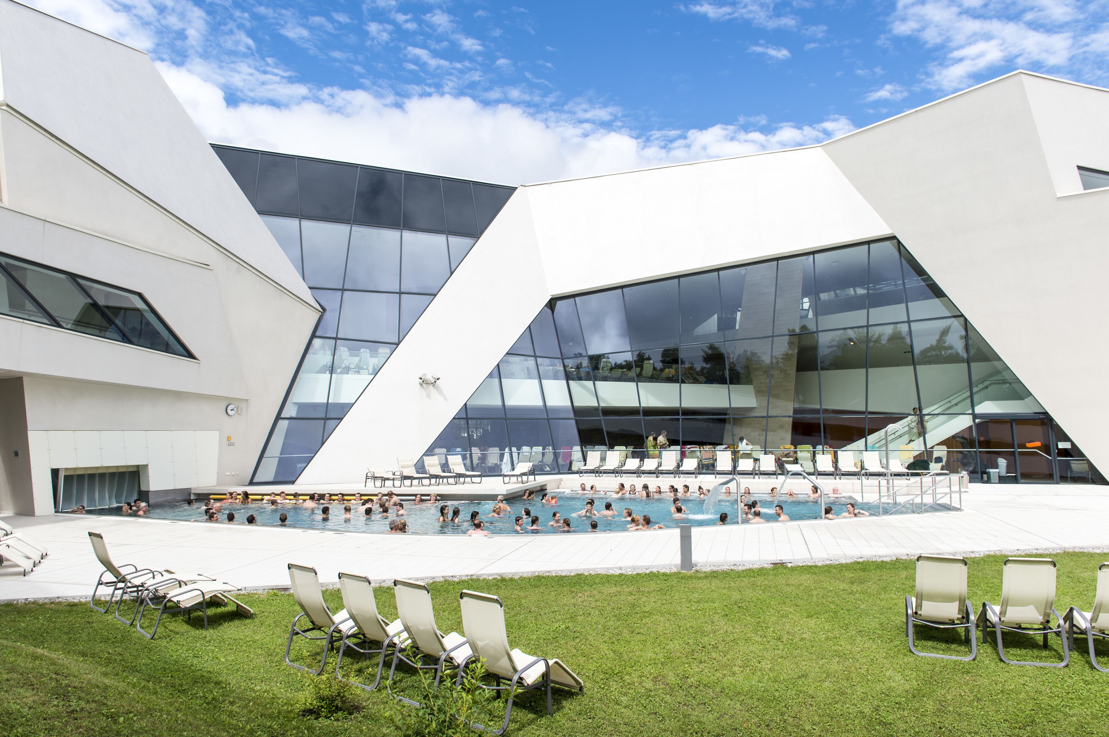 Un edifici modern amb una gran façana de vidre i una zona de piscina amb gandules.