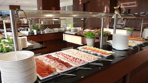 A buffet with various food options, including meats and salads, arranged on a counter with a glass cover. - Thermenhotel Karawankenhof (Villach)