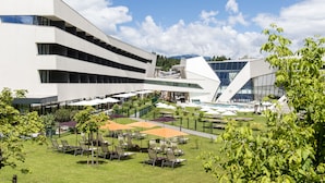 A modern building with a courtyard featuring outdoor seating and umbrellas. - Thermenhotel Karawankenhof (Villach)