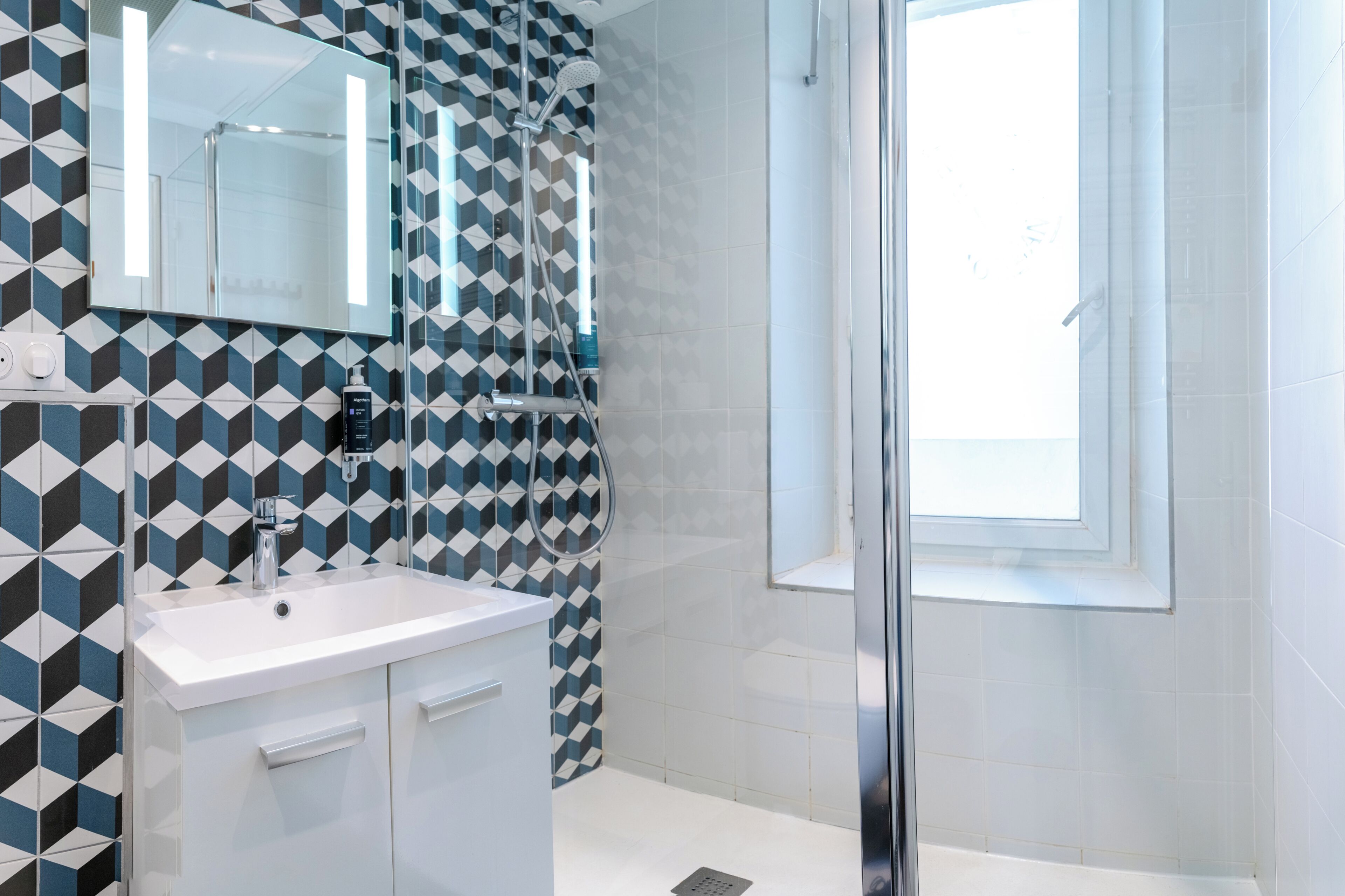 A bathroom with a geometric patterned wall, a white sink, and a glass shower enclosure.