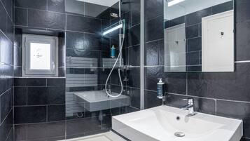 Un baño moderno con un lavamanos blanco, una ducha con cerramiento de vidrio y un espejo sobre el lavamanos.