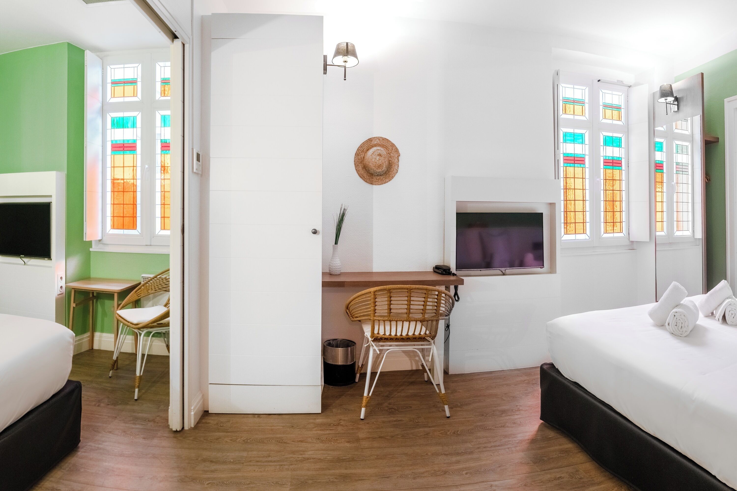 A hotel room with a bed, a desk with a chair, a TV, and a window with stained glass.