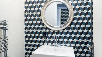 A bathroom with a geometric patterned wall, a round mirror, a white sink, and a chrome towel rack.