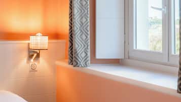 Een hotelkamer met een bed, nachtkastje, lamp, raam met gordijnen en uitzicht op de omgeving.