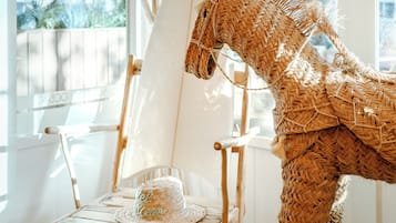 Una escultura de caballo de mimbre, un sombrero de mimbre y una silla de madera en una habitación con una ventana blanca y otra silla blanca.