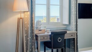 A room with a desk, chair, lamp, and a TV on the wall. - Hôtel de L'Océan et Restaurant - Coeur de Ville (Biarritz)