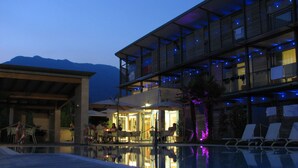 A modern hotel with a pool, outdoor seating, and a mountain backdrop. - Park Hotel Il Vigneto (Arco)