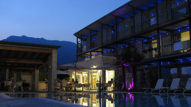 A modern hotel with a pool, outdoor seating, and a mountain backdrop. - Park Hotel Il Vigneto (Arco)