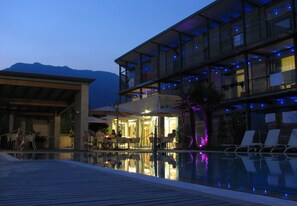 Un hotel moderno con piscina, mobiliario de exterior y montañas al fondo.